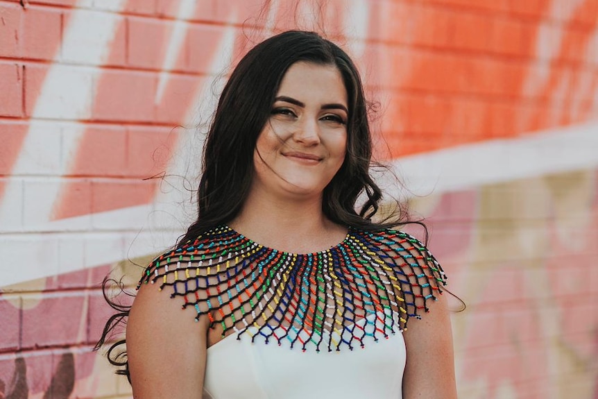 A brown-haired woman standing in front of a graffitti wall.