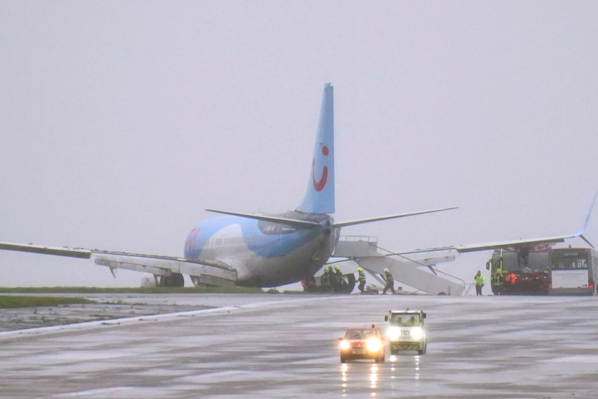 A blue plane skids off the runway on a rainy day