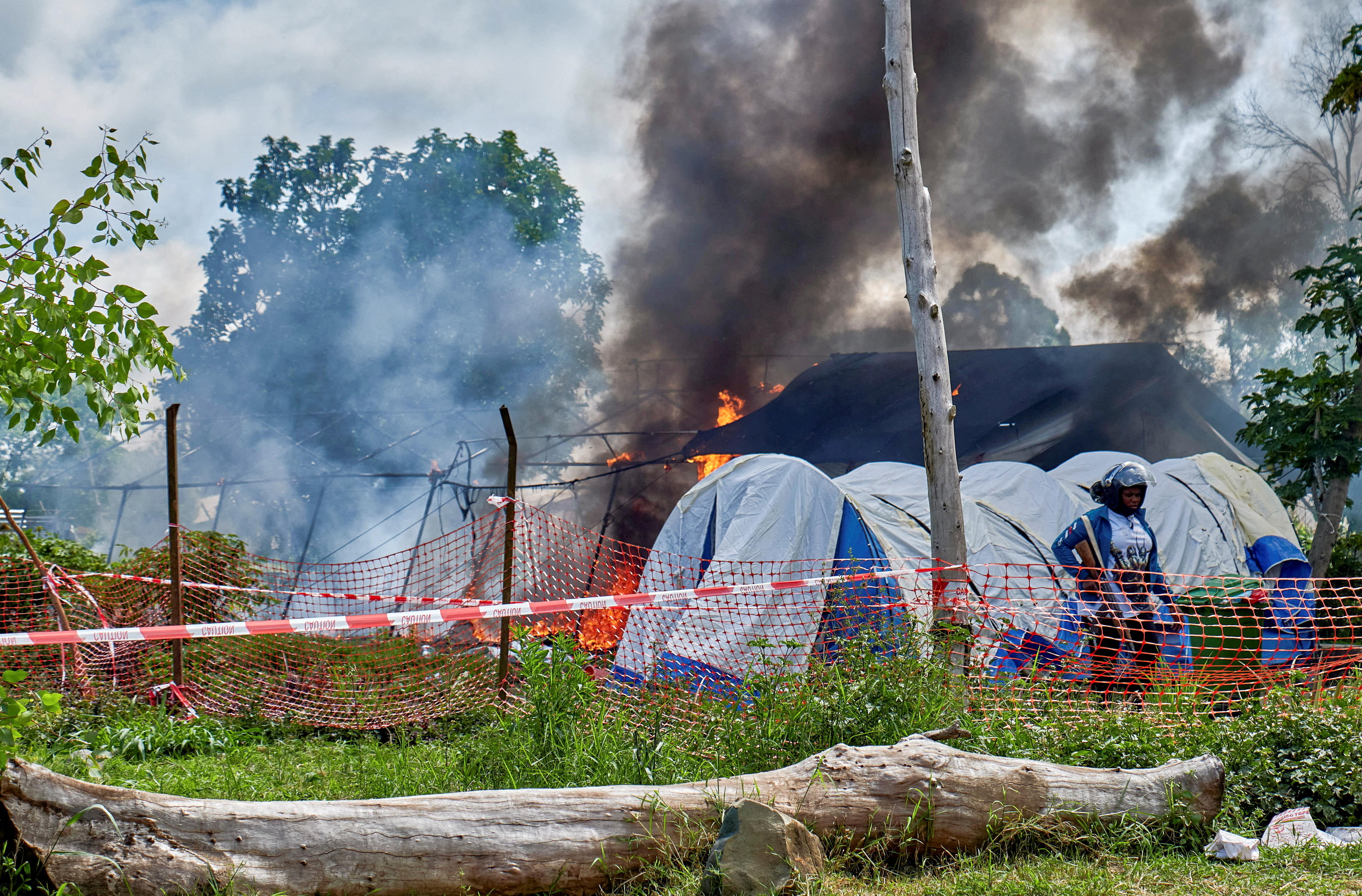 Medical tents burn behind a Congolese police officer in the middle of the day.