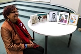 Marlene Jackamarra sits in a chair with pictures of her relatives sitting on a table beside her.