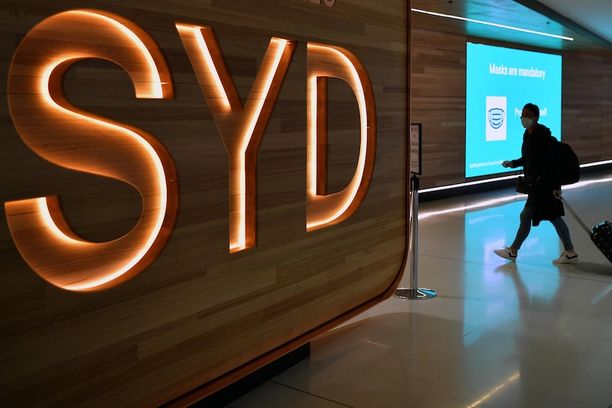 A passenger walks next to a departures sign at Sydney International Airport