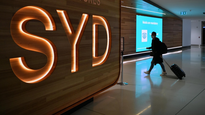 A passenger walks next to a departures sign at Sydney International Airport