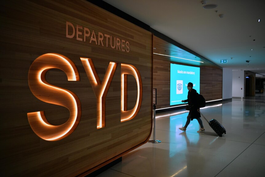 A passenger walks next to a departures sign at Sydney International Airport