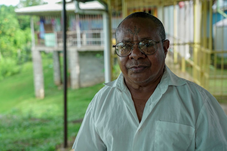 A Papua New Guinean man in a white shirt stands on a balcony