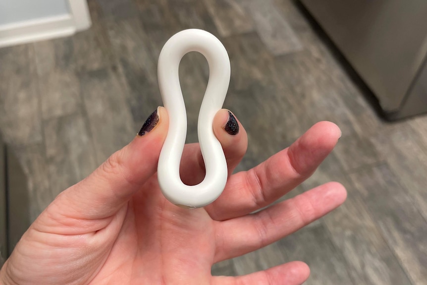 A woman squishing a white vaginal ring into an almost figure eight position