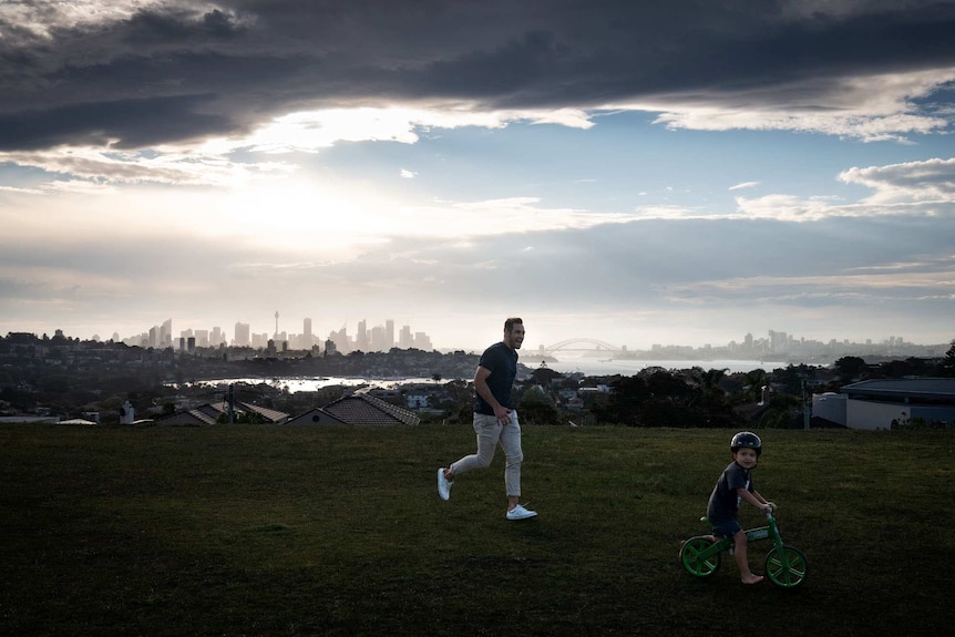 Father and son play in a park with a backdrop of Sydney Harbour.