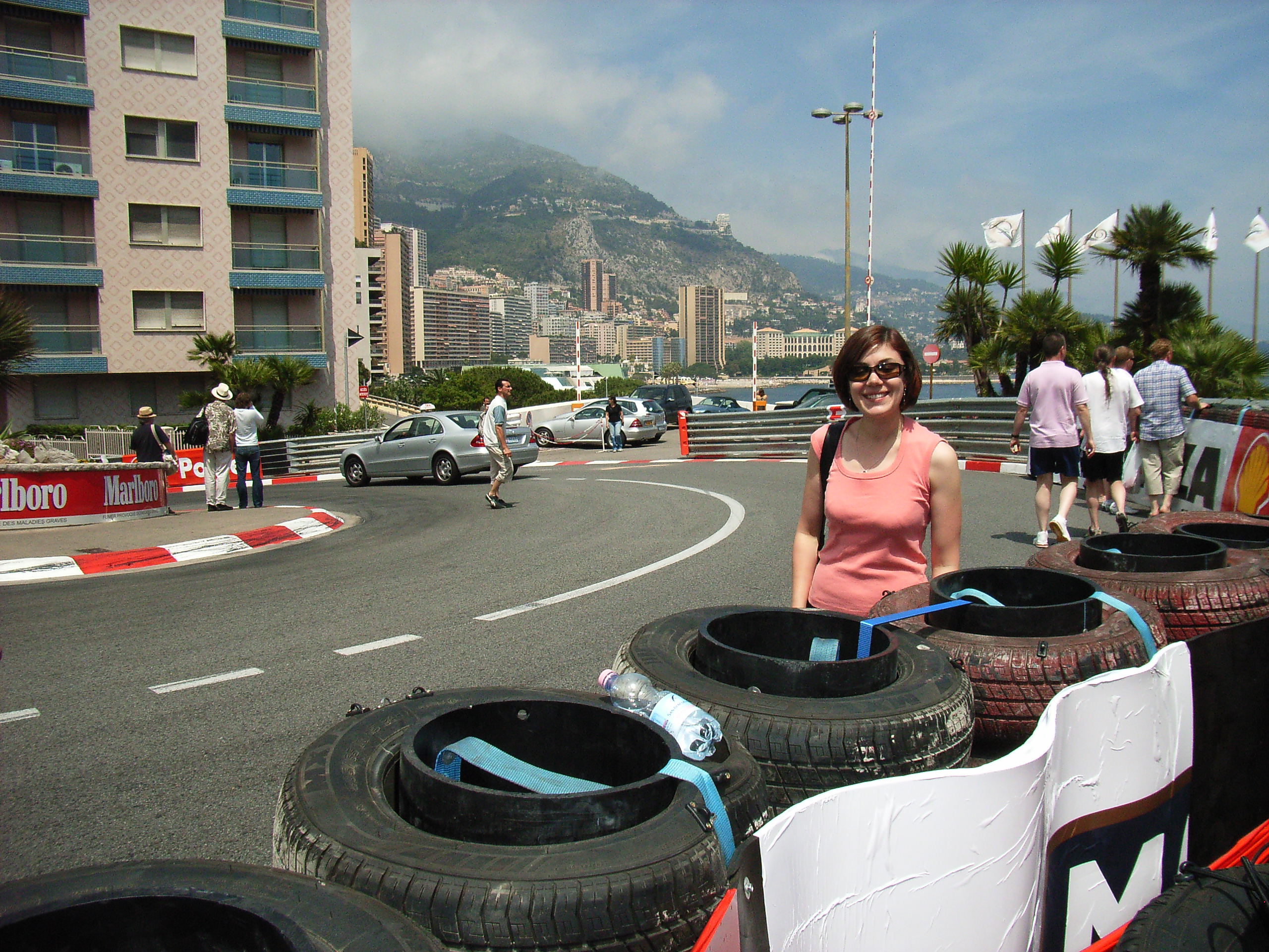 A young woman in sunglasses and pink tank top stands on a road in a European city