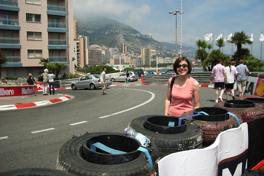 A young woman in sunglasses and pink tank top stands on a road in a European city