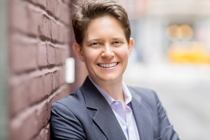 Portrait of woman with short hair standing outside, smiling, against a brick wall. 