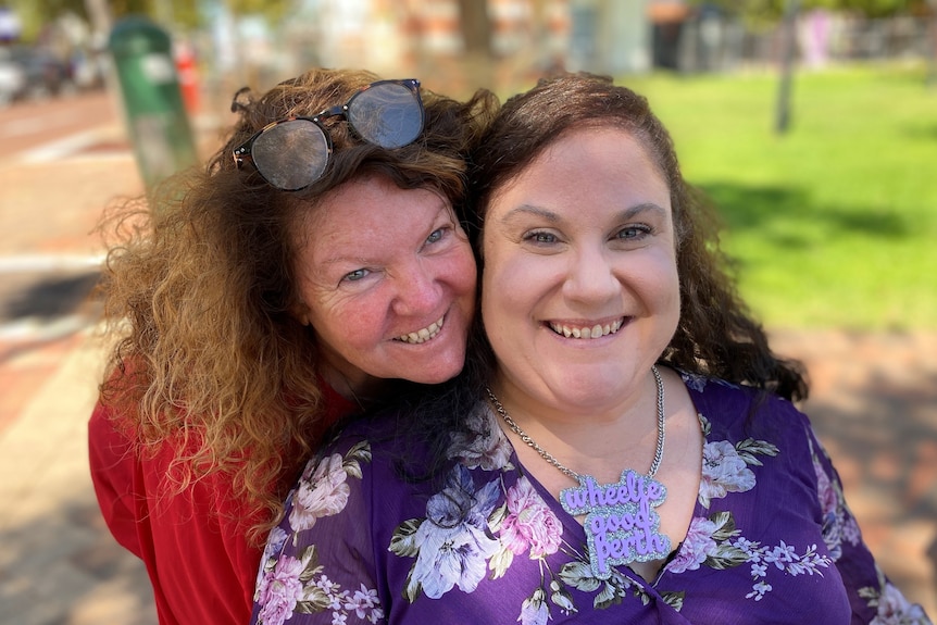 A woman in a purple dress smiles cheek to cheek with a woman in read