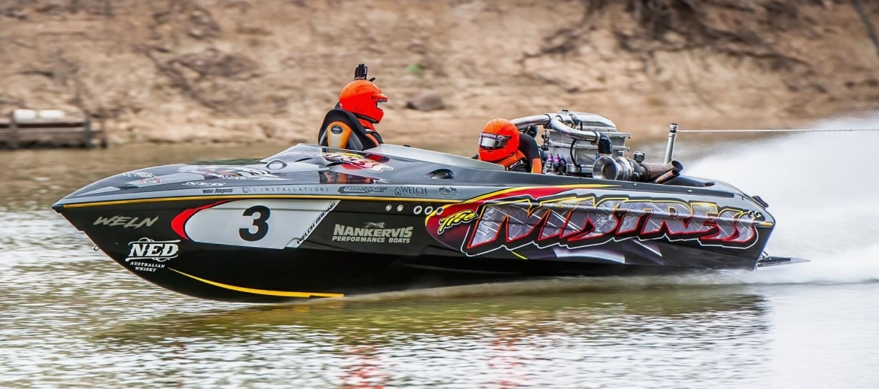 Dos hombres con cascos naranjas recorren un río en una lancha negra