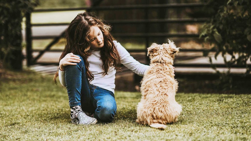 A girl sits on the lawn next to her dog for a story about what to do when the family pet dies.