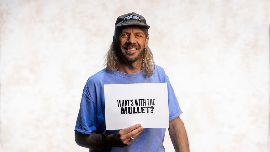 Man holding a sign 'what's with the mullet'?