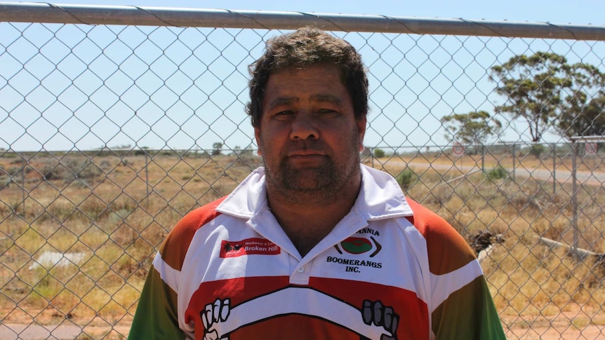 A man wearing a rugby shirt standing in front of a chain link fence.