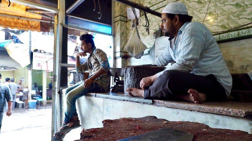 Indian butchers sit idle in Nizamuddin and are surrounded by rows of empty hooks as they watch the crowd go by