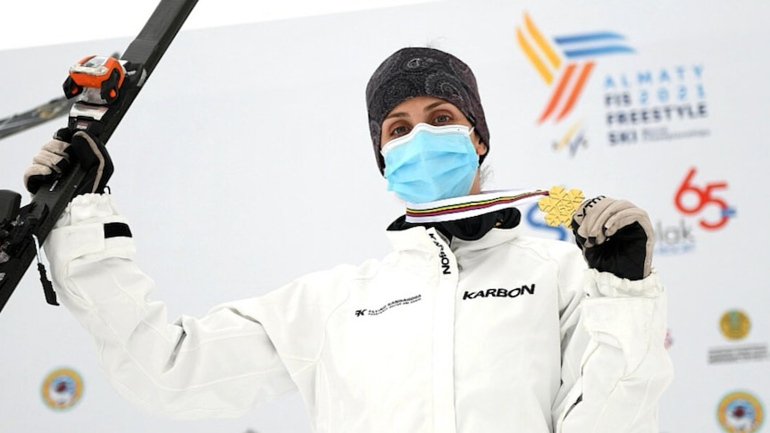 An aerial skier stands with her ski in one hand an a gold medal in the other after a world title.