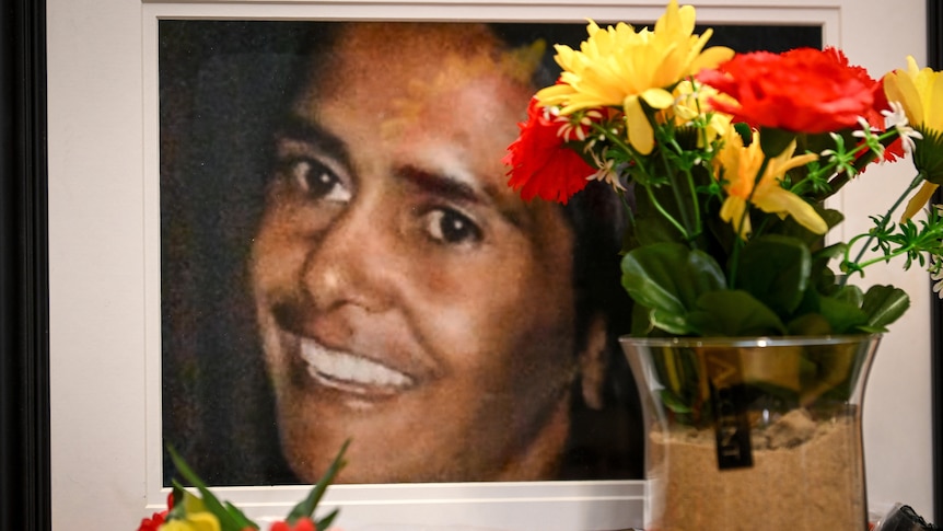 A photo of a woman's smiling face next to a vase of bright-coloured flowers.