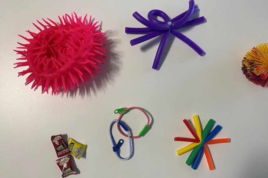 kit contents including coloured fidget toys, sour lollies, zip toys, stress balls and rubber bands spread out on a white surface