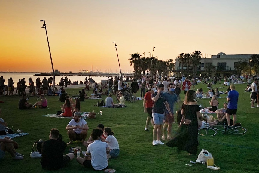 Large groups of people on the grass at sunset at St Kilda beach.