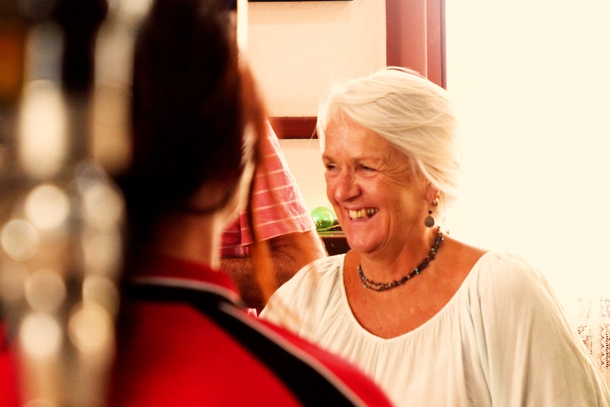 A woman with grey hair laughing, with an out-of-focus beer in the foreground.