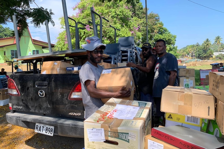 Men in PNG unload boxes off a ute tray
