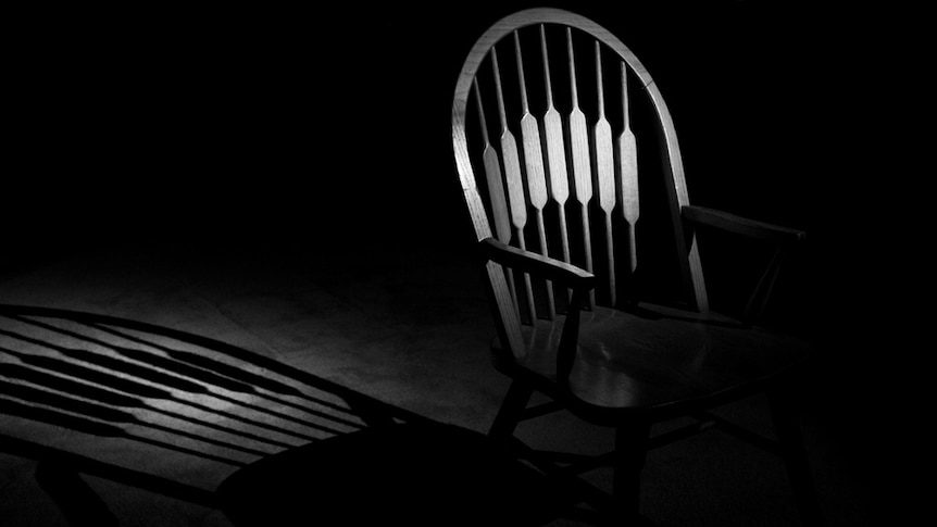 An empty chair casts a shadow in a darkened room