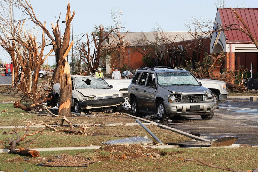 People walk near cars and trees damaged by a tornado at the Canadian Valley Technology Center in El Reno, Oklahoma.