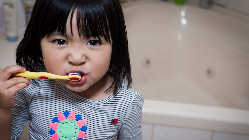A young girl brushes her teeth in a bathroom