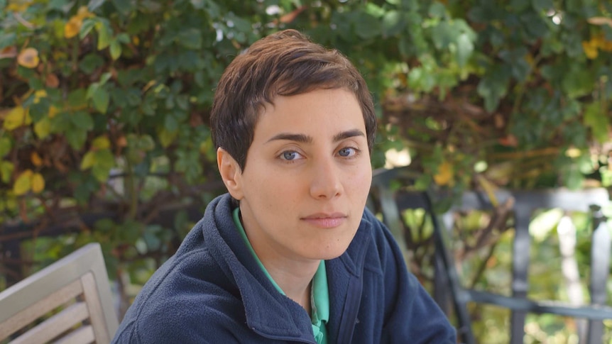 Maryam Mirzakhani seated on a bench in a garden setting.