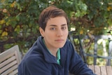 A close-up of Maryam Mirzakhani seated on a bench in a garden setting.