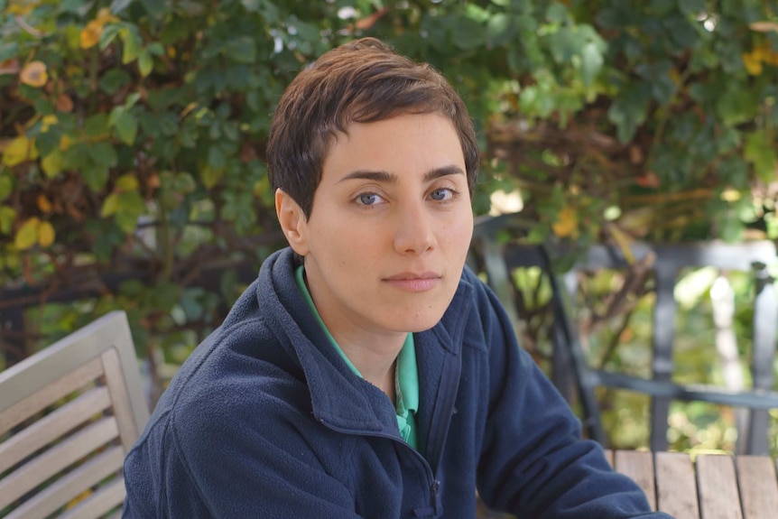 A close-up of Maryam Mirzakhani seated on a bench in a garden setting.