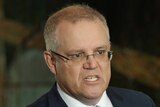 Scott Morrison bares his teeth and points a finger while talking. There are microphones around him.