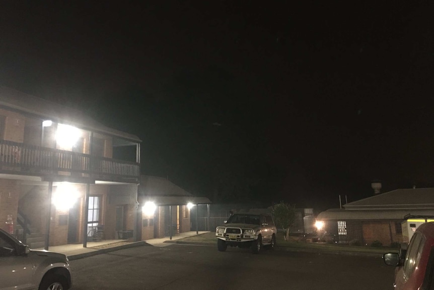 A motel in night-like darkness caused by smoke. Only building lights show the motel's car park.