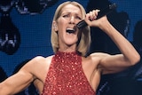 A woman with shoulder-length blonde hair, wearing a glittery red dress, sings powerfully into a microphone