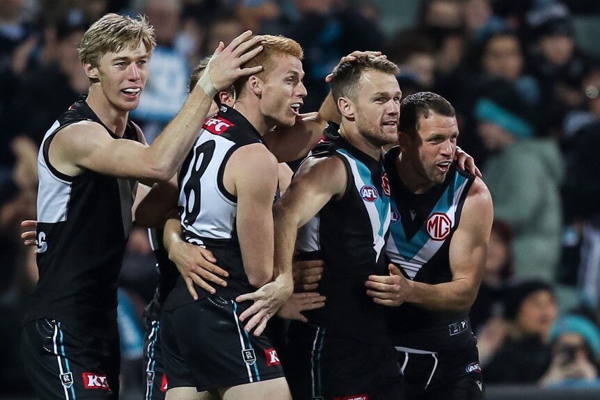 A group pf Port Adelaide AFL players embrace as they celebrate a goal.