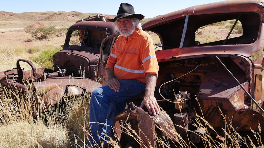 An aboriginal man sitting on old weathered cars during the day at an aboriginal community.