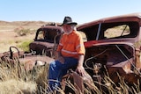 An aboriginal man sitting on old weathered cars during the day at an aboriginal community.