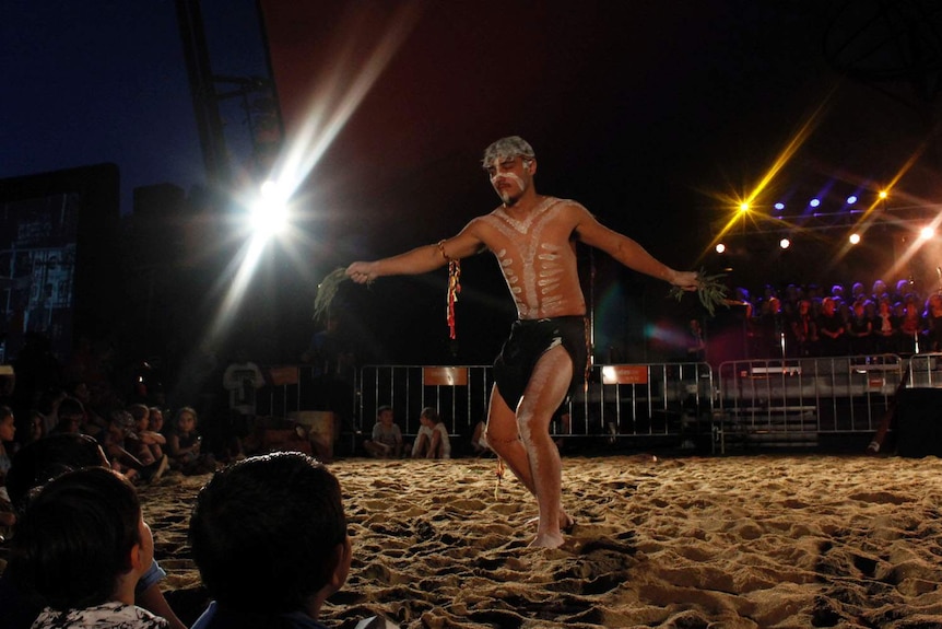 An aboriginal man with white markings painted on his body, dancing, holding gum leaves.