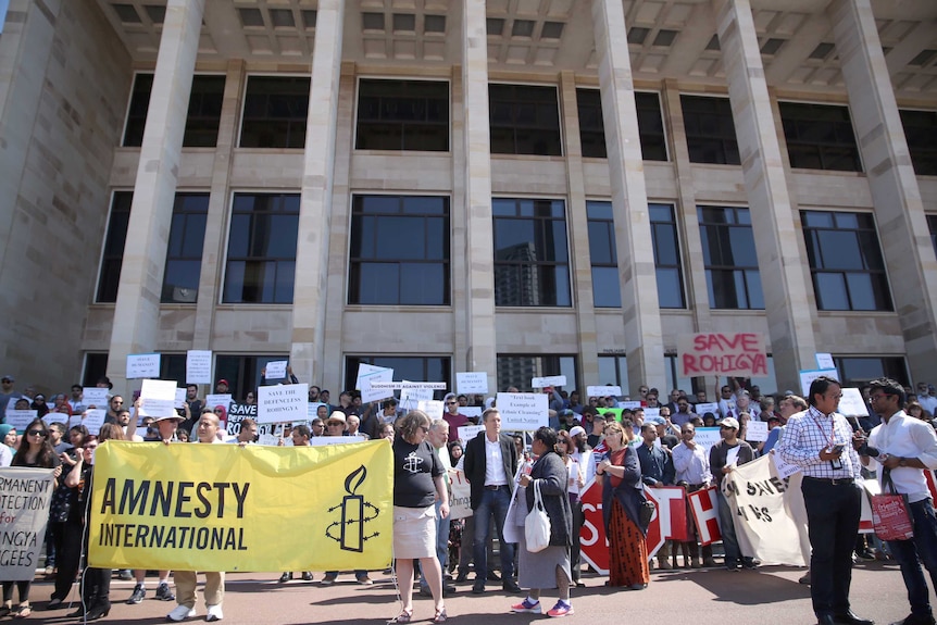 A group of people holding banners stand on the steps of parliament house.