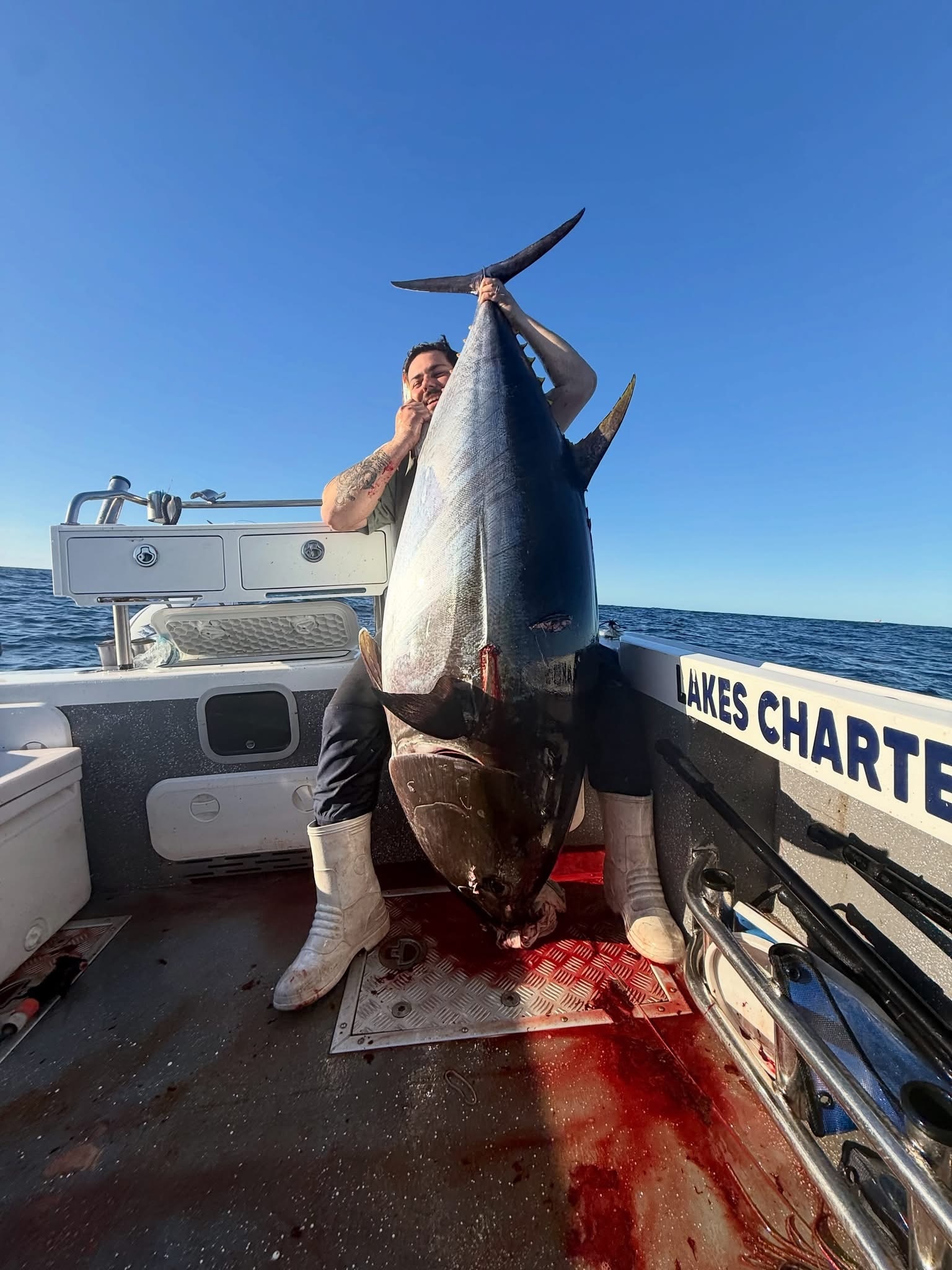 A man sitting on a boat holding a giant tuna fish, ocean in the background