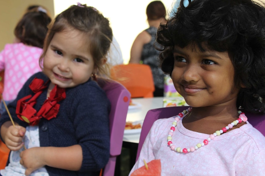 Two little girls sit smiling and playing together.