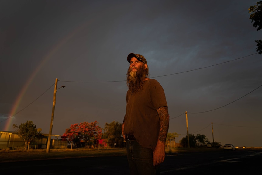 Man stands in the street, dark clouds and rainbow in the background.