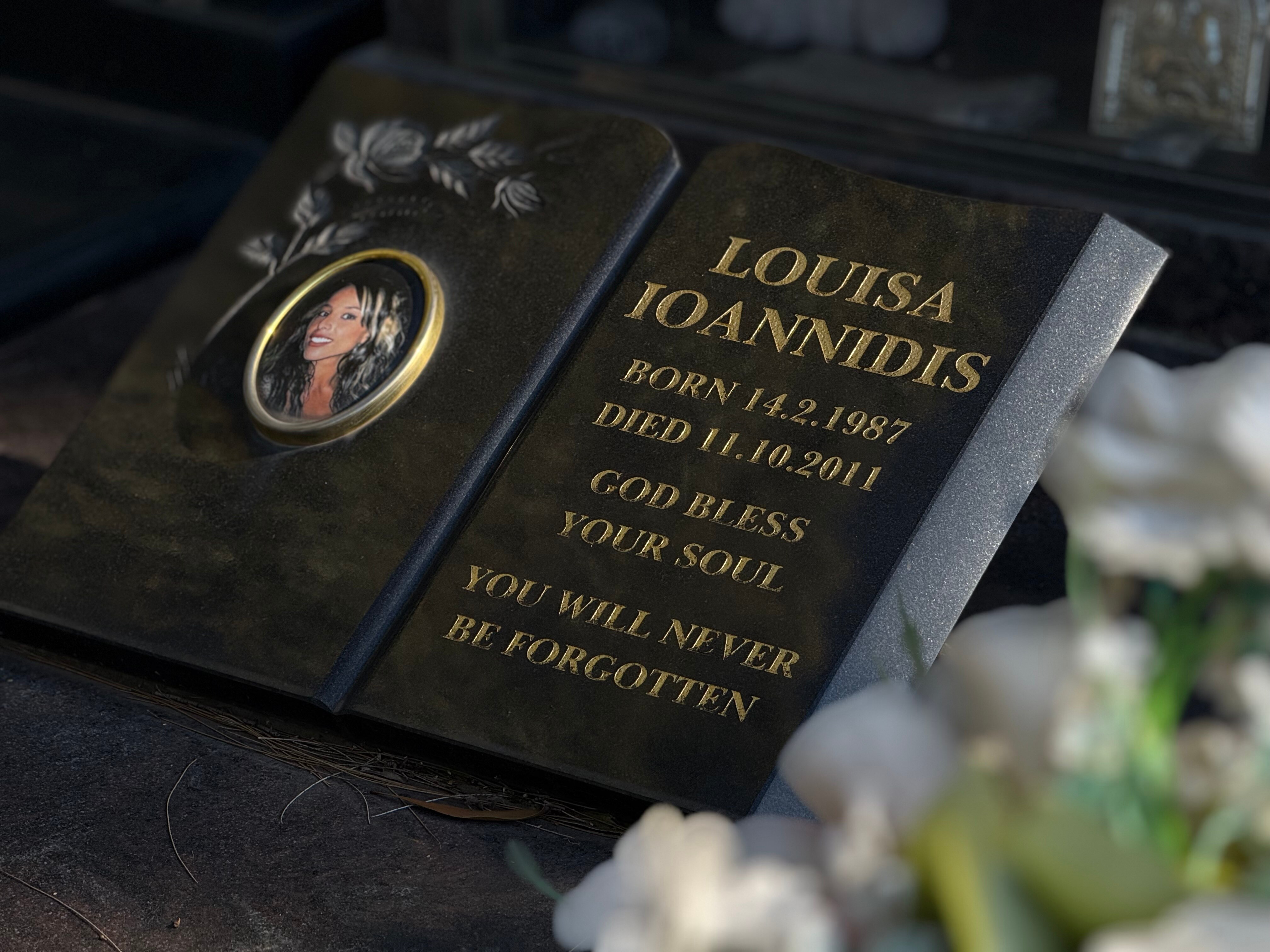 A dark marble grave stone showing a picture of a young smiling woman with dark hair. Grave of Louisa Ioannidis 