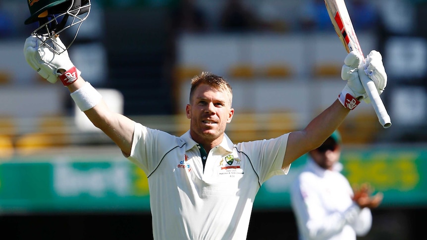 David Warner holds his bat and helmet aloft with a big smile on his face.