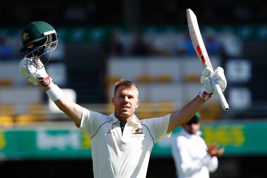 David Warner holds his bat and helmet aloft with a big smile on his face.
