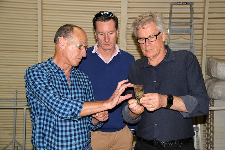 Three men examine a core drilling sample.