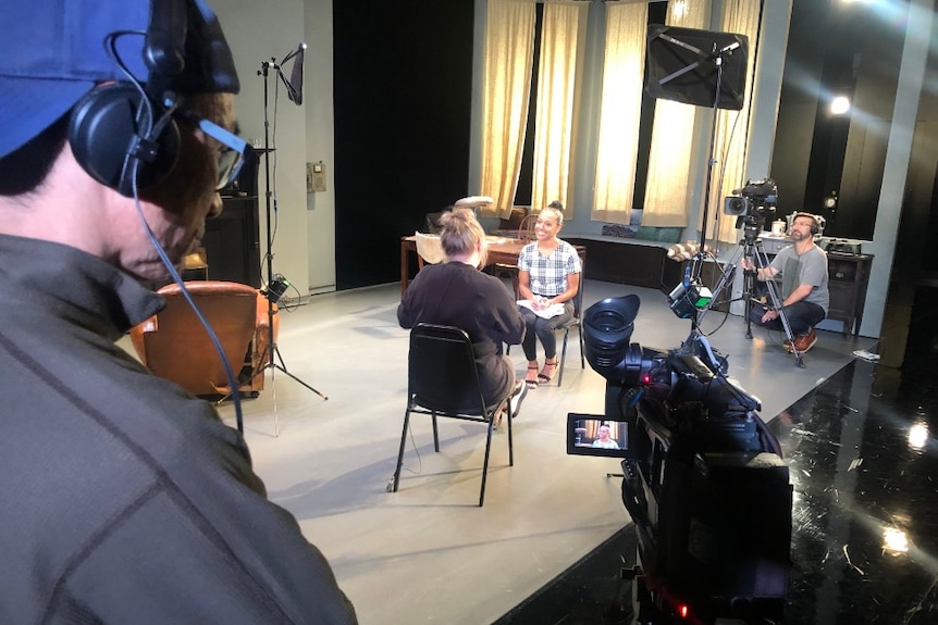 Cameras and lights surrounding Corowa sitting on chair interviewing woman.