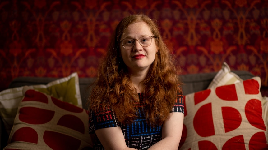 A woman sitting on a couch with red cushions and wallpaper