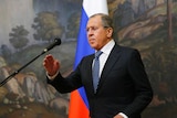 Russian Foreign Minister Sergey Lavrov is seen preparing to speak, behind him a Russia flag and a wall mural.