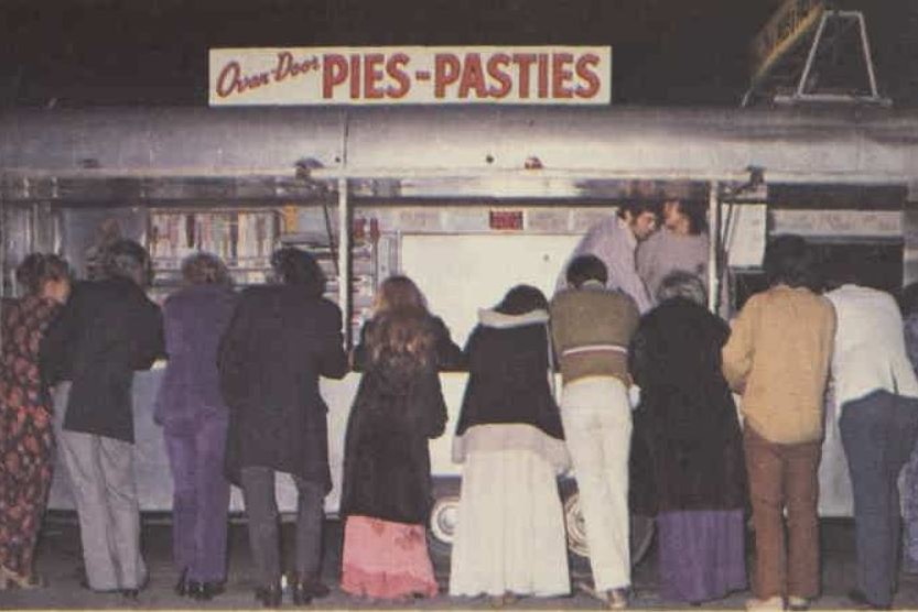 A picture from the 1970s of people seen from behind lined up at a pie cart.